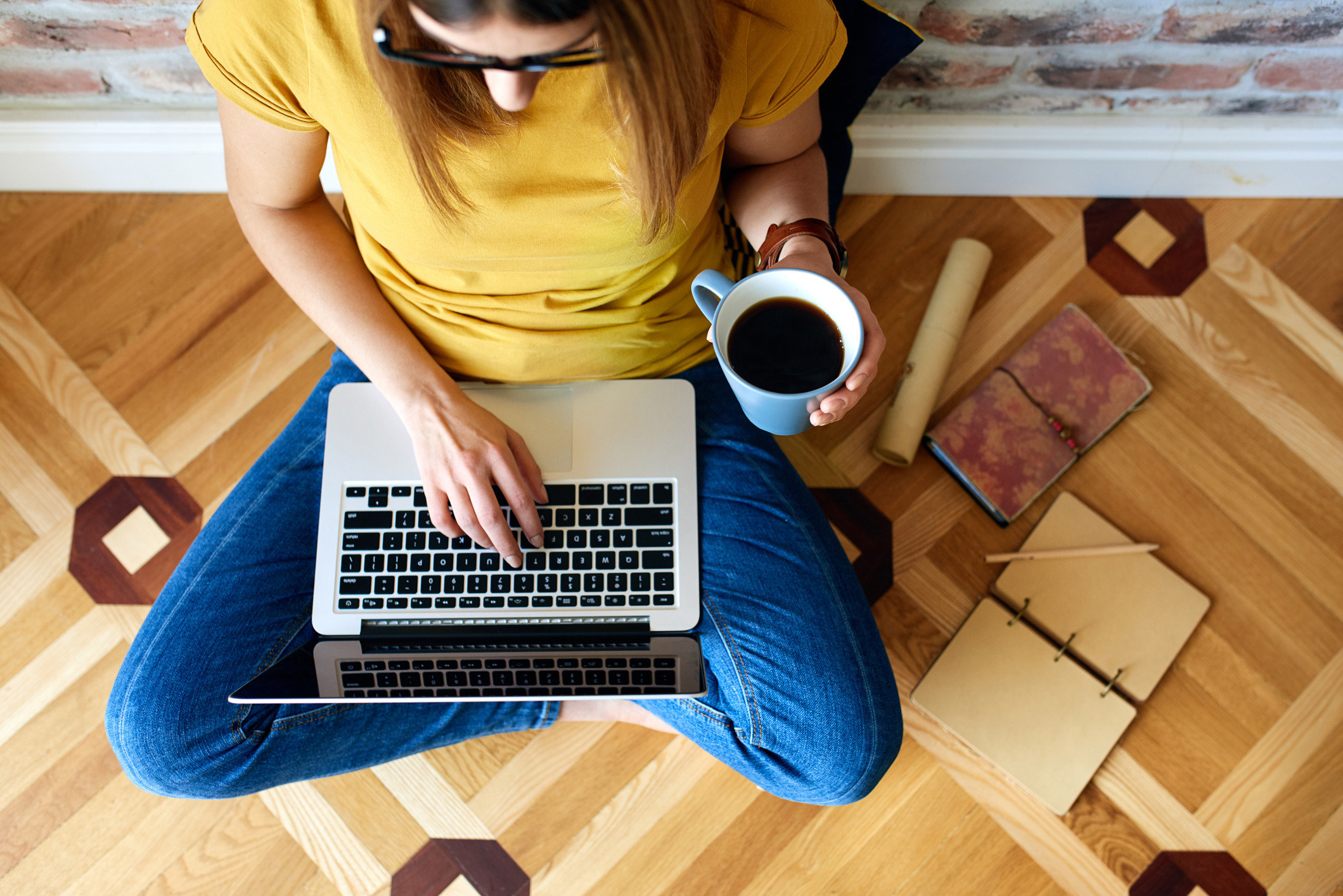 Shot van boven vrouw met laptop en koffie in geel tshirt