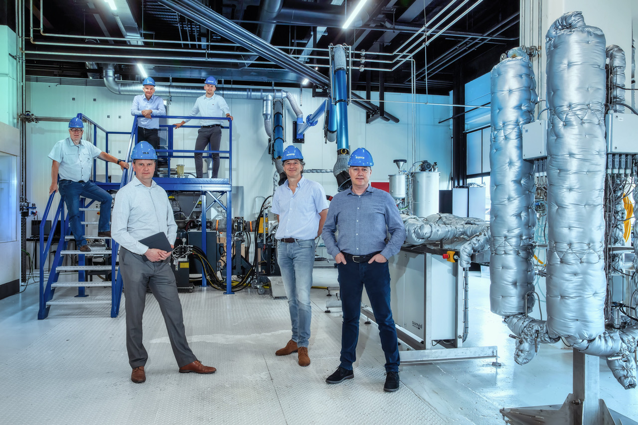 Foto van zes mannen met blauwe helmen in fabriek met blauwe en zilveren apparaten