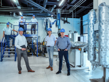Foto van zes mannen met blauwe helmen in fabriek met blauwe en zilveren apparaten